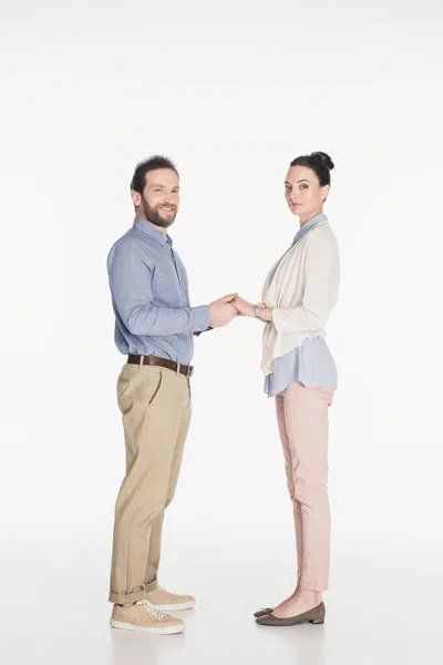 Вид сбоку супружеской пары, держащейся за руки и вместе смотрящей в камеру на белом фоне — стоковое фото