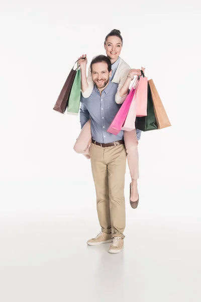 Happy woman with shopping bags and husband piggybacking together isolated on white — Stock Photo