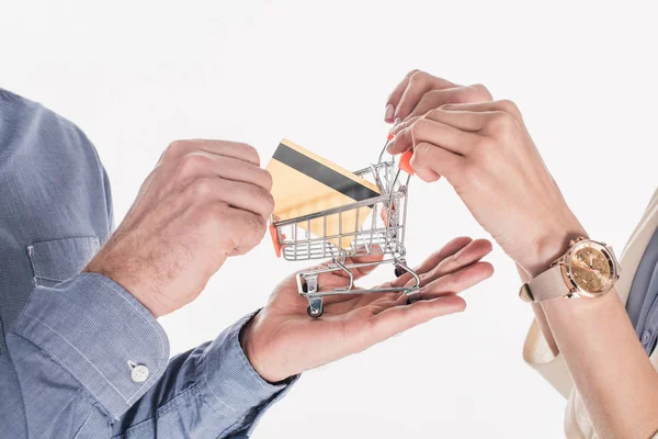 Recortado disparo de pareja sosteniendo poco carrito de la compra y tarjeta de crédito en las manos aisladas en blanco - foto de stock