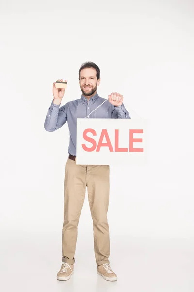 Sonriente hombre con tarjeta de venta y tarjeta de crédito en manos aisladas en blanco - foto de stock