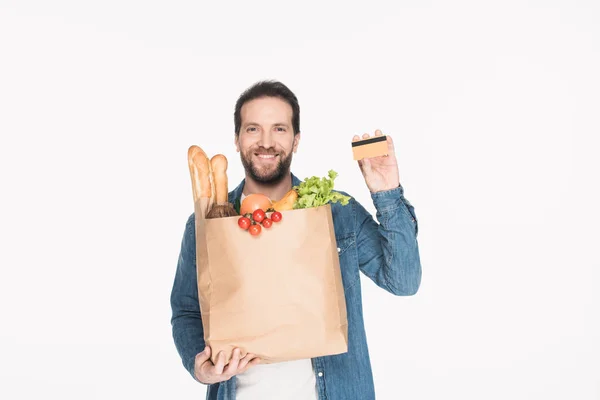 Портрет улыбающегося мужчины с кредитной картой и бумажной упаковкой, полной еды, изолированной на белом — стоковое фото