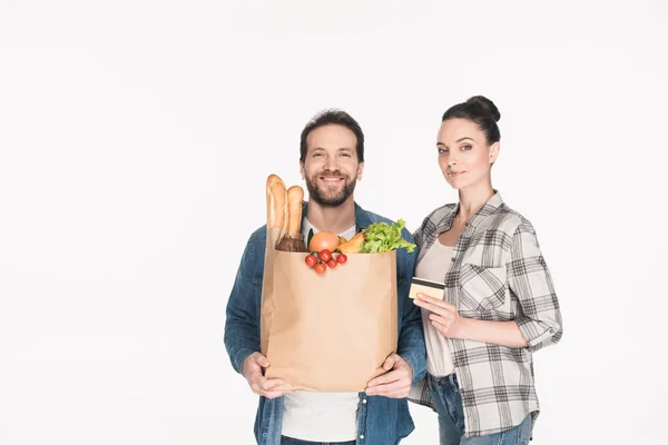 Retrato de casal sorridente com cartão de crédito e pacote de papel com supermercado isolado em branco — Fotografia de Stock