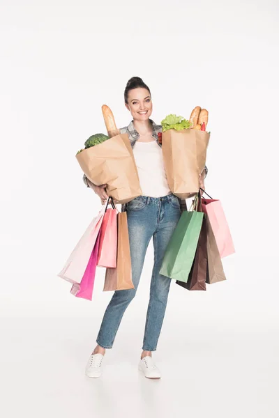 Mujer alegre sosteniendo paquetes de papel con comida y bolsas de compras en manos aisladas en blanco - foto de stock