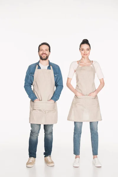 Smiling shop assistants in aprons looking at camera isolated on white — Stock Photo