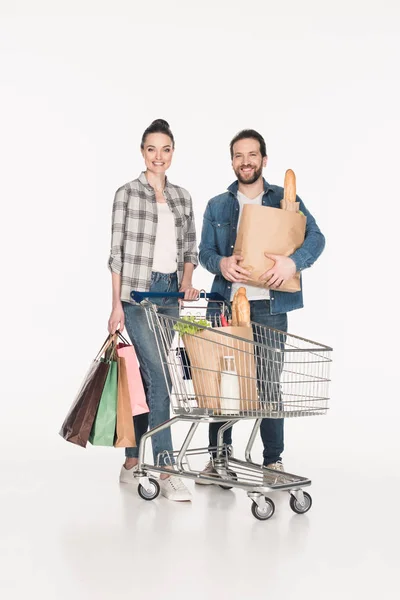 Glückliches Paar mit Einkaufstaschen, Papierpaketen mit Lebensmitteln und Einkaufswagen isoliert auf weiß — Stockfoto