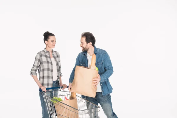 Esposa y marido con paquetes de papel llenos de comida y carrito de compras aislados en blanco - foto de stock
