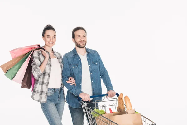 Porträt eines lächelnden Paares mit Einkaufstaschen und Papierpaketen mit Lebensmitteln im Einkaufswagen isoliert auf weiß — Stockfoto