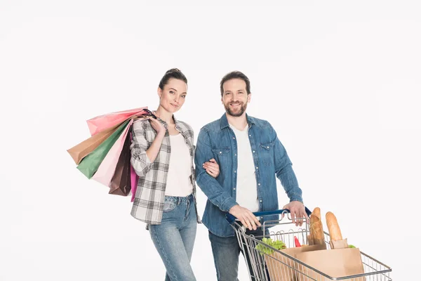 Porträt eines lächelnden Paares mit Einkaufstaschen und Papierverpackungen voller Lebensmittel in einem Einkaufswagen isoliert auf weiß — Stockfoto