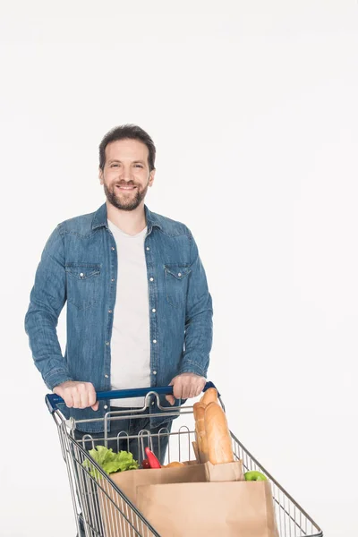 Ritratto di uomo sorridente con carrello pieno di pacchi di carta con cibo isolato su bianco — Foto stock