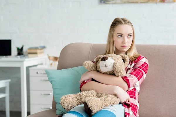 Красива дівчина-підліток обіймає свого плюшевого ведмедя, сидячи на дивані — стокове фото