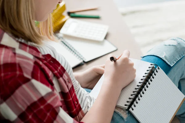 Cropped shot of teen student girl writing in notebook while sitting on couch — Stock Photo