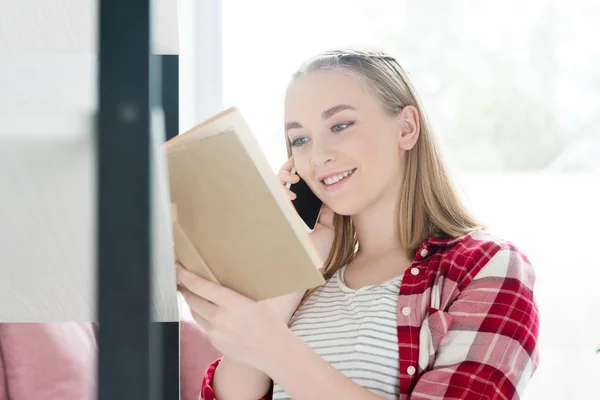 Ritratto ravvicinato di una studentessa sorridente che legge un libro e parla per telefono — Foto stock