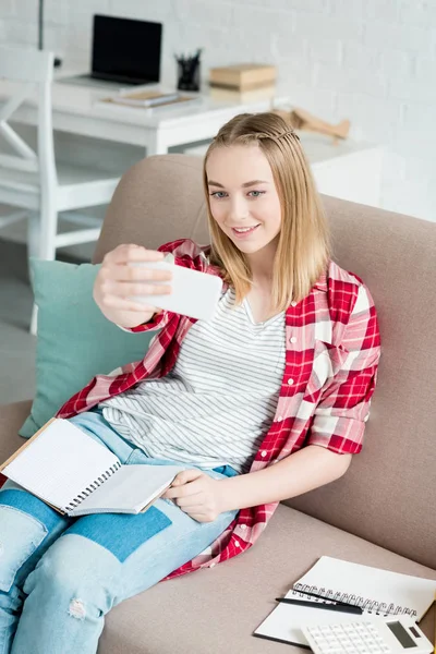 Teenager-Studentin mit Notizbuch sitzt auf Couch und macht Selfie — Stockfoto