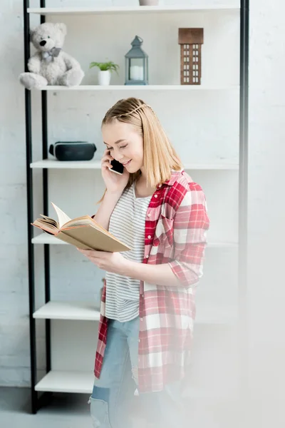 Happy teen student girl reading book and talking by phone — Stock Photo