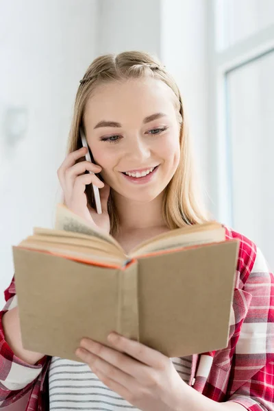 Nahaufnahme Porträt eines glücklichen Teenie-Studentenmädchens, das Buch liest und telefoniert — Stockfoto