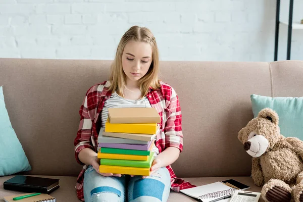 Adolescente studentessa con pila di libri seduta sul divano — Foto stock