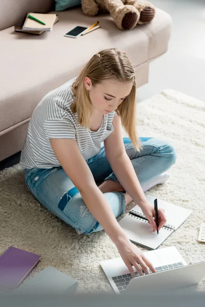 Vista de ángulo alto de adolescente estudiante haciendo tarea mientras está sentado en el suelo - foto de stock