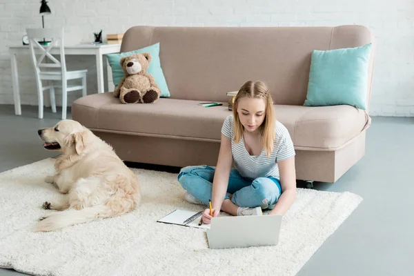 Підліток студент дівчина робить домашнє завдання, сидячи на підлозі зі своєю собакою — стокове фото