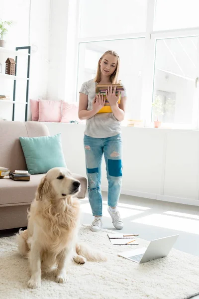 Belle adolescente avec pile de livres étudiant à la maison avec son golden retriever — Photo de stock