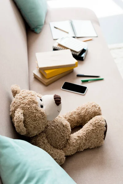 Visão de alto ângulo de ursinho de pelúcia no sofá com material escolar em casa — Fotografia de Stock