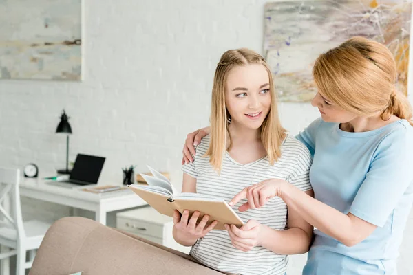 Mother and teen daughter reading book together at home — Stock Photo