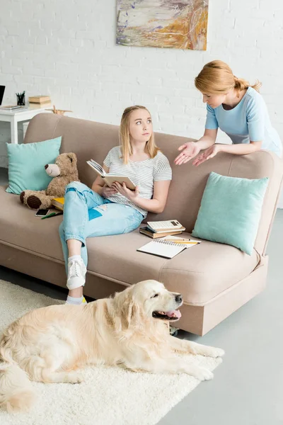 Mãe ensinando sua filha em casa enquanto ela faz lição de casa e seu cão deitado no chão — Fotografia de Stock