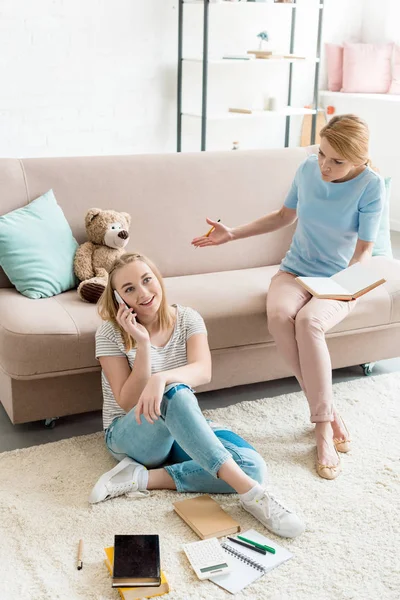 Мать заставляет дочь учиться, пока она разговаривает по телефону — стоковое фото