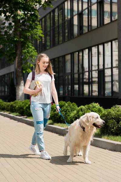 Teen student girl with books walking her dog — Stock Photo