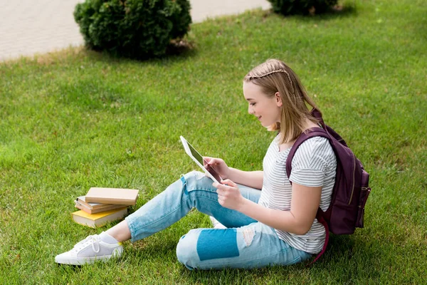 Підліток студент дівчина використовує планшет, сидячи на траві — стокове фото