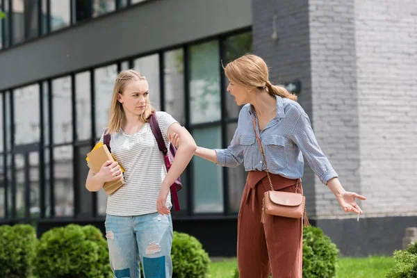 Mère tirant sa fille et forçant à aller quelque part alors qu'elle tient une pile de livres — Photo de stock