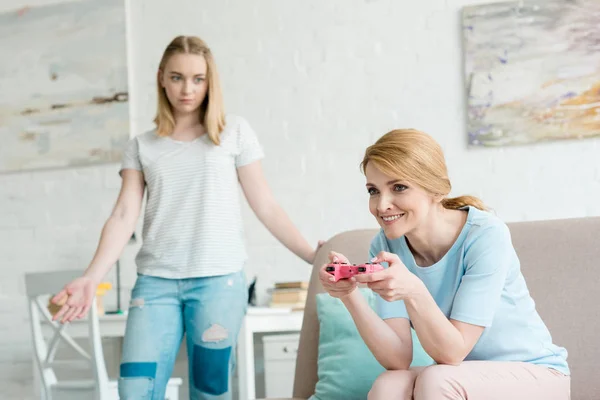 Confuso adolescente filha olhando para a mãe enquanto ela joga consola jogo — Fotografia de Stock