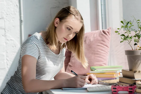 Centrado adolescente estudiante chica haciendo tarea en windowsill - foto de stock