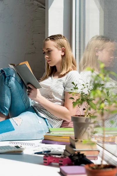 Adolescent étudiant fille lecture livre tandis que assis sur le rebord de la fenêtre — Photo de stock