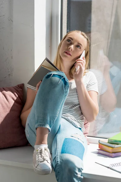 Adolescente estudiante chica sentado en windowsill y hablando por teléfono - foto de stock