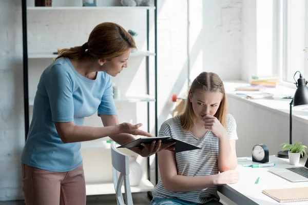 Frightened teen daughter sitting on chair while her mother yelling and showing notebook — Stock Photo