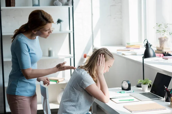 Depressed teen daughter sitting at work desk at home while her mother yelling at her — Stock Photo