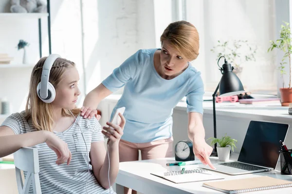 Mutter zwingt ihre Tochter Hausaufgaben zu machen, während sie mit Kopfhörern Musik hört — Stockfoto