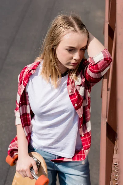 Pensativo adolescente chica en rojo camisa a cuadros con monopatín - foto de stock