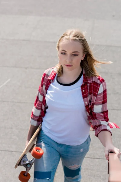 Linda menina adolescente em camisa xadrez vermelho andando com skate na mão — Fotografia de Stock