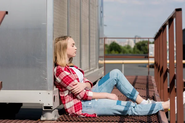 Vue latérale de réfléchie teen girl en chemise à carreaux rouge assis sur le toit — Photo de stock