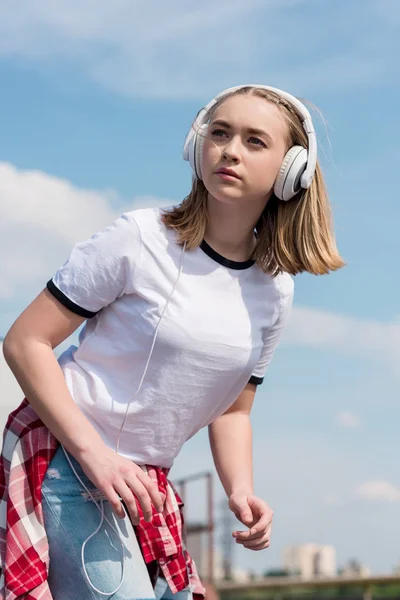 Красива дівчина-підліток в навушниках перед блакитним небом — стокове фото