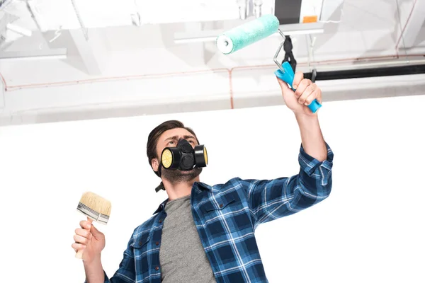 Vue à faible angle de l'homme dans le respirateur travaillant par rouleau de peinture et pinceau — Photo de stock