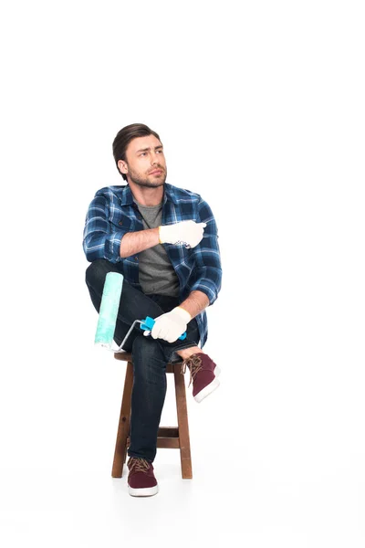 Uomo in guanti protettivi seduto sulla sedia con rullo di vernice isolato su sfondo bianco — Foto stock