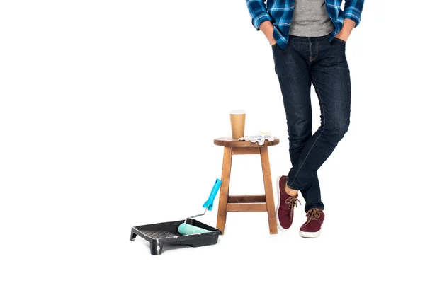 Cropped shot of man standing near chair with protective gloves, coffee cup and roller tray with paint roller isolated on white background — Stock Photo