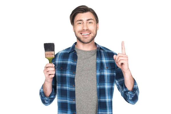 Sonriente hombre sosteniendo pincel de pintura y haciendo gesto de idea aislado sobre fondo blanco - foto de stock