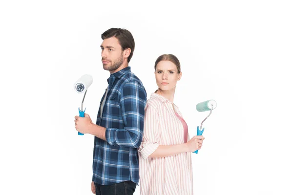 Jeune couple avec des rouleaux de peinture debout dos à dos isolé sur fond blanc — Photo de stock