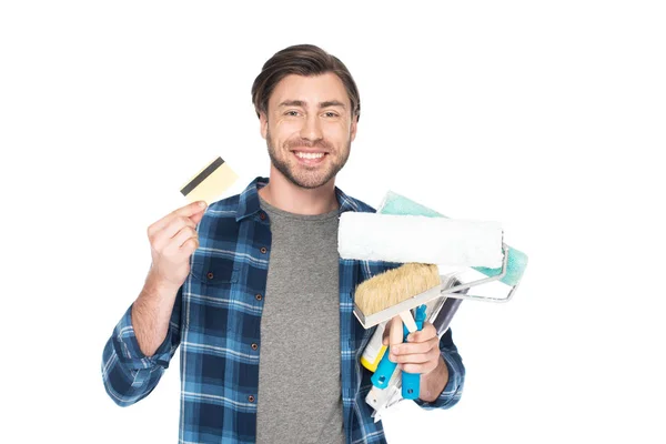 Homme souriant avec carte de crédit tenant rouleaux de peinture et pinceau isolé sur fond blanc — Photo de stock