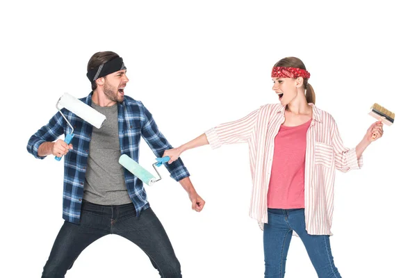 Vue latérale du couple hurlant dans les bandeaux se battant par des rouleaux de peinture isolés sur fond blanc — Photo de stock