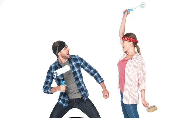Gritando casal em headbands lutando por rolos de pintura isolados no fundo branco — Fotografia de Stock