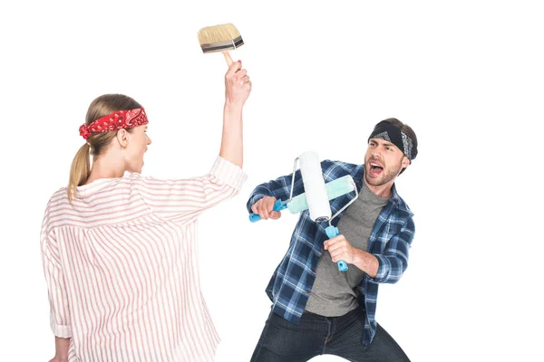 Rückansicht einer schreienden Frau, die ihren Freund mit dem Pinsel angreift, während er sich mit zwei Farbrollen vor weißem Hintergrund schützt — Stockfoto